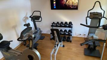 Un gimnasio en casa con diferentes equipos de ejercicio, incluyendo una elíptica, una bicicleta estática y una prensa de banca.