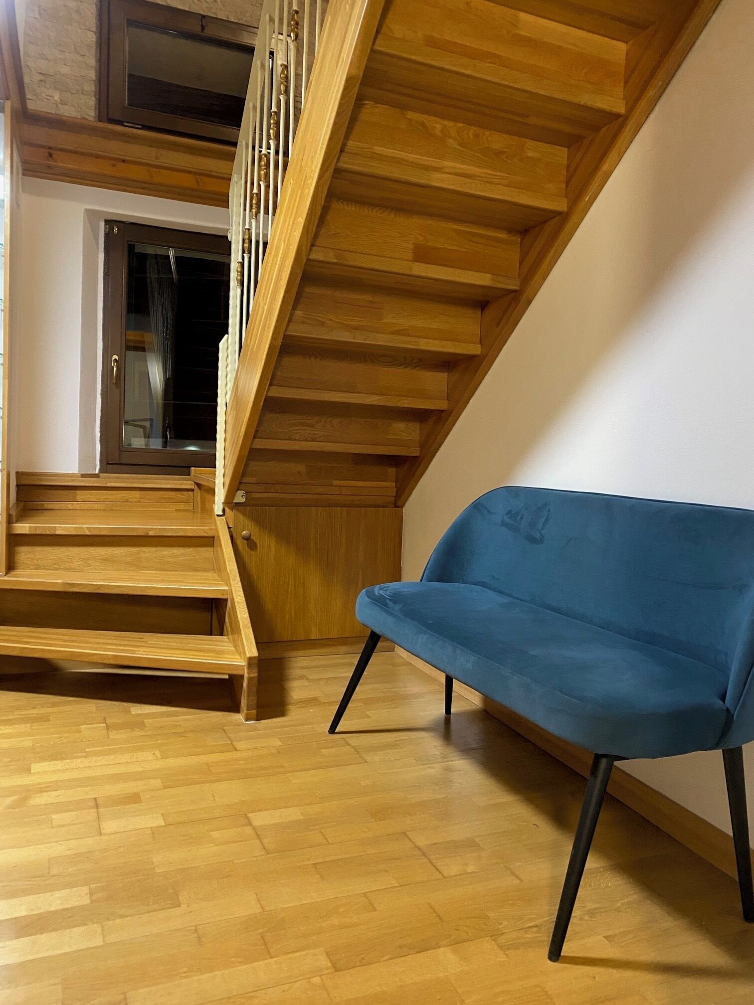 A wooden staircase leading to an upper floor, a blue chair, and a wooden floor.