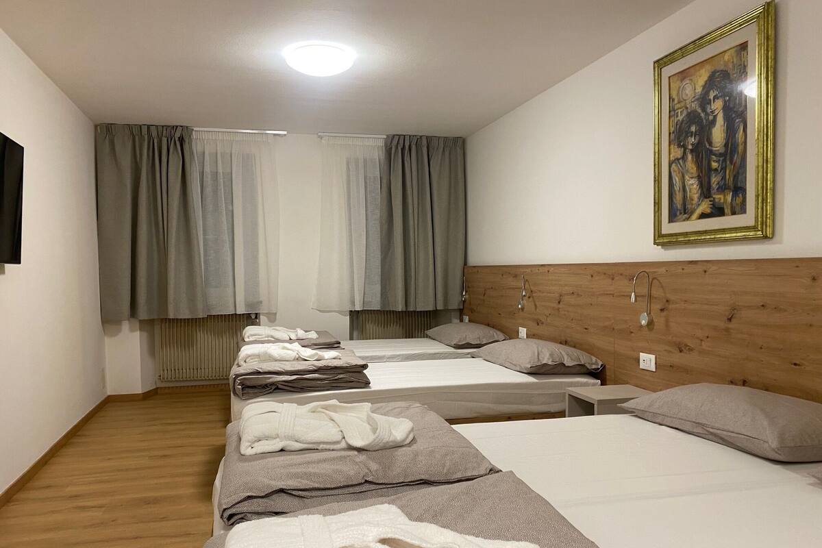 A hotel room with three beds, a wooden headboard, a painting on the wall, and a radiator under the windows.
