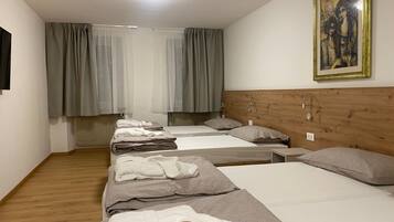 Ein Hotelzimmer mit drei Betten, einem Holzkopfende, einem Gemälde an der Wand und einer Heizung unter den Fenstern.