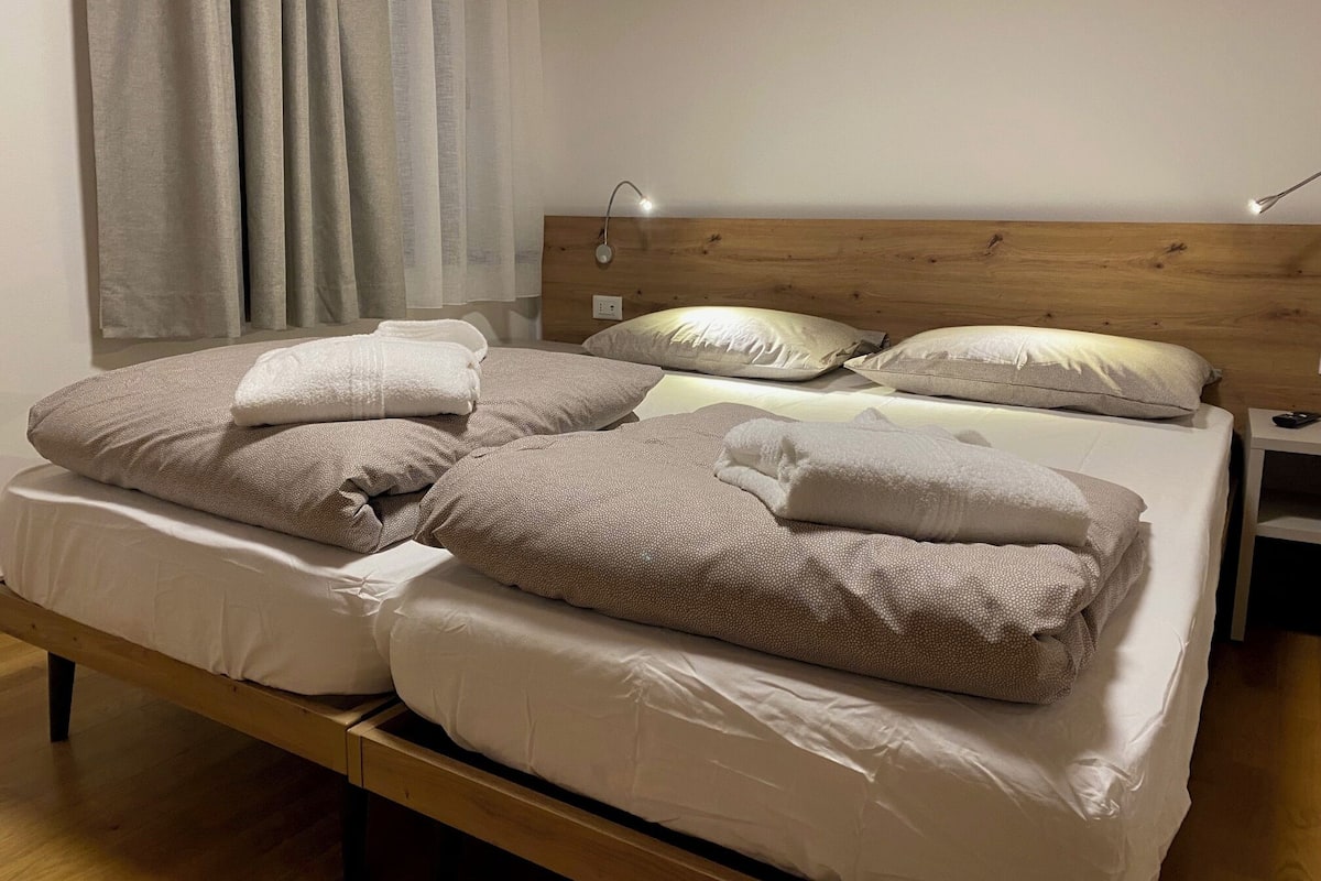 A neatly made bed with white and beige bedding, a wooden headboard, and a bedside table with a lamp.