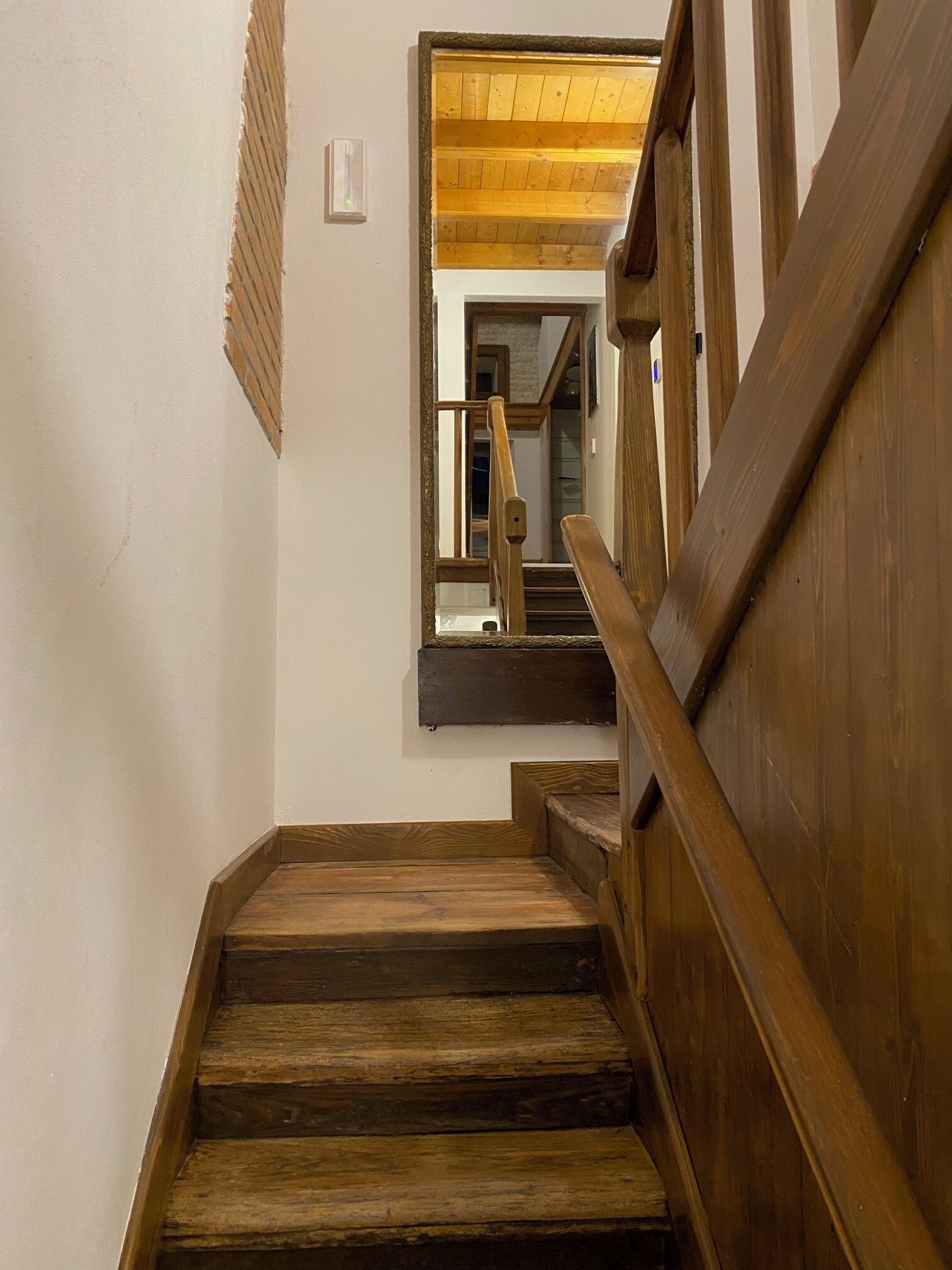 Una escalera de madera con barandilla que lleva a una habitación con techo de madera y una ventana.