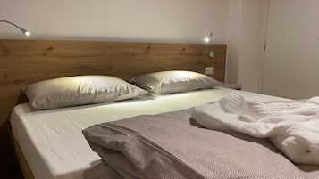 En snyggt bäddad säng med en trägavel, två kuddar och en hopvikt filt.