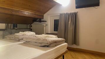 Une chambre avec un plafond en bois, un lit avec une literie blanche, une fenêtre avec des rideaux et un téléviseur à écran plat fixé au mur.