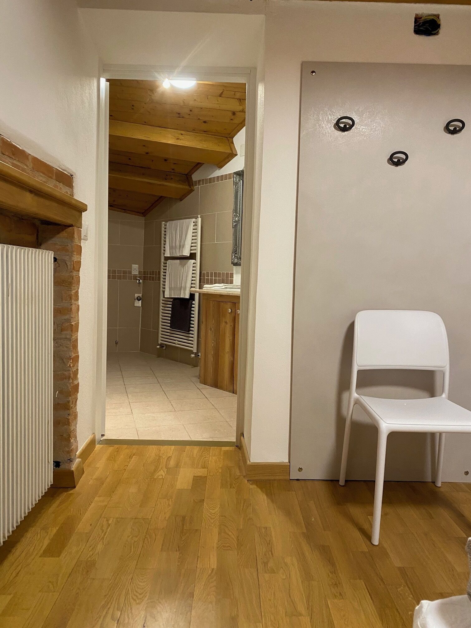 A hallway leading to a kitchen with a radiator, wooden floor, and a white chair.