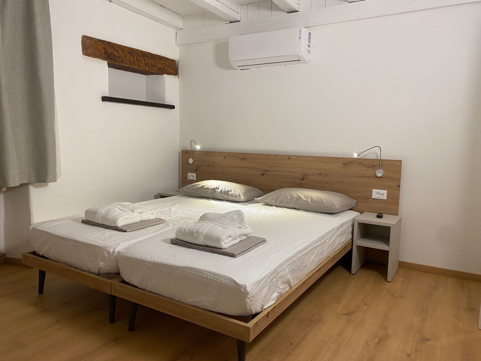 Un letto matrimoniale con testiera in legno, due comodini e un condizionatore d'aria a parete.