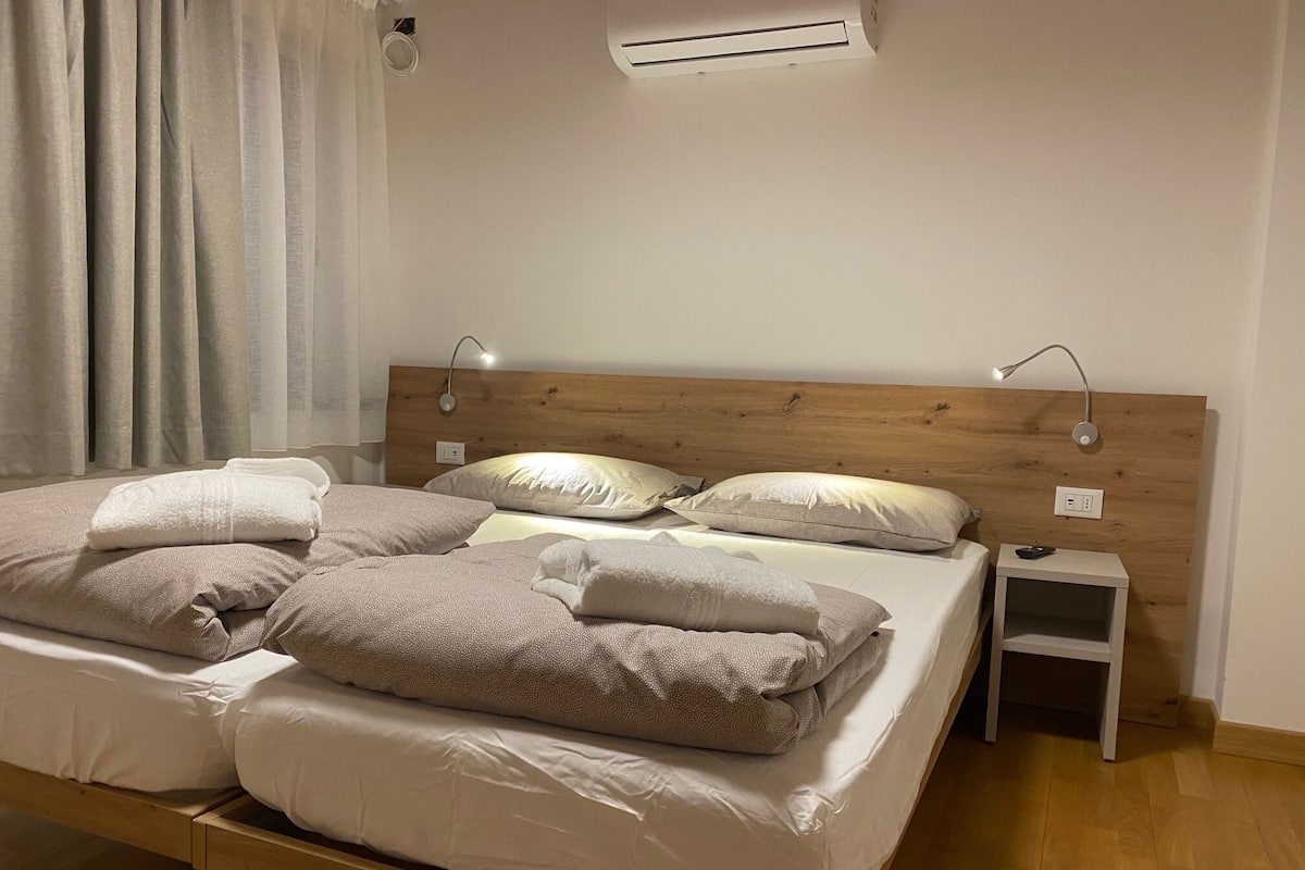 A double bed with a wooden headboard, two bedside tables, and a wall-mounted air conditioner.