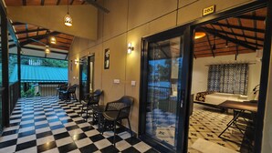 A hotel corridor with a checkered floor, seating area with chairs, and a room with a bed and patterned curtains. - Ibex Resorts Malampuzha Kava Eco Camp (Malampuzha-I)