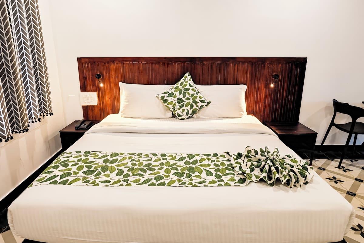 Una cama bien hecha con una colcha de estampado de hojas, un cabecero de madera y una mesita de noche con un teléfono.