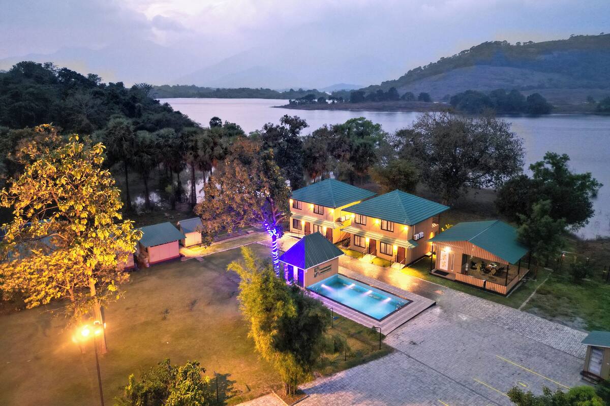 Una casa grande con piscina, rodeada de árboles y un lago.