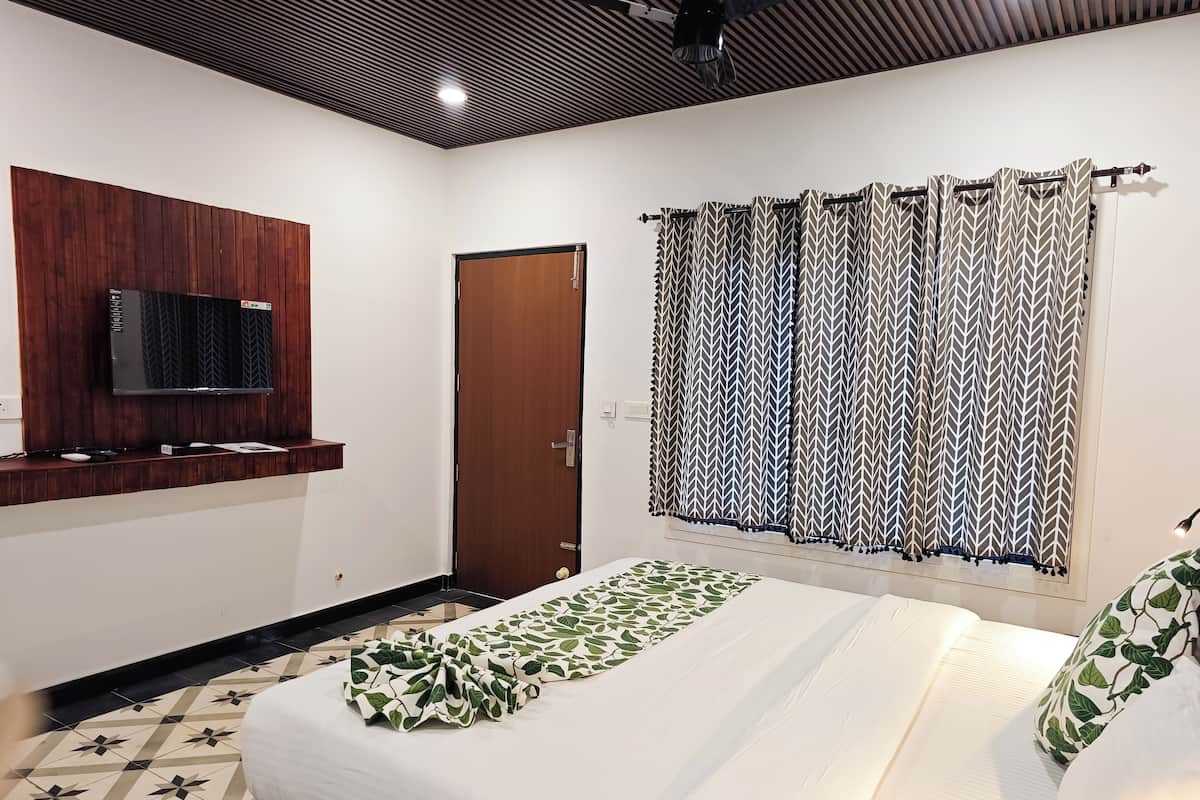 Una habitación de hotel con una cama, un televisor montado en un panel de madera, una cortina estampada y un piso con diseño.