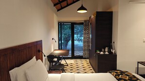 A bedroom with a bed, a desk, and a chair. There is a window with a view of trees and a balcony. - Ibex Resorts Malampuzha Kava Eco Camp (Malampuzha-I)
