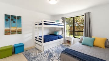 A bedroom with a bunk bed, a bedside table, a window with curtains, a rug, and a painting on the wall.