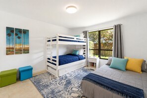 Een slaapkamer met een stapelbed, een nachtkastje, een raam met gordijnen, een vloerkleed en een schilderij aan de muur.