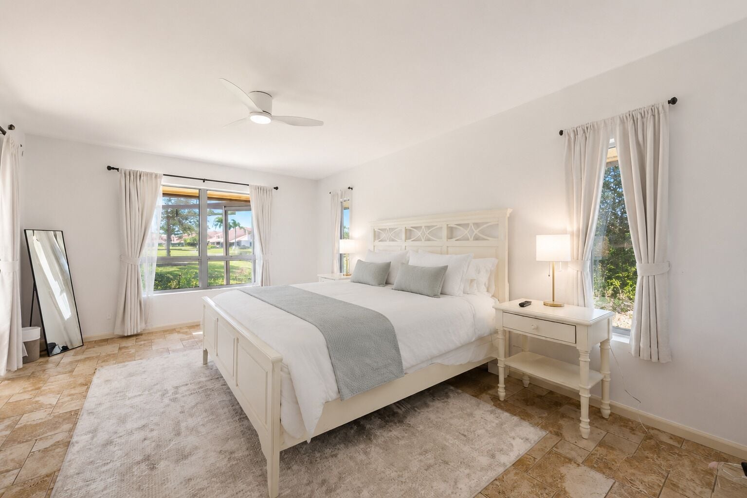 Een slaapkamer met een bed, nachtkastjes, een spiegel en een raam met gordijnen.