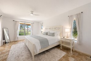 Une chambre à coucher avec un lit, des tables de chevet, un miroir et une fenêtre avec des rideaux.
