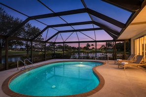 Une piscine dotée d’une enceinte en verre, entourée de chaises longues et offrant une vue sur un terrain de golf et un plan d’eau.