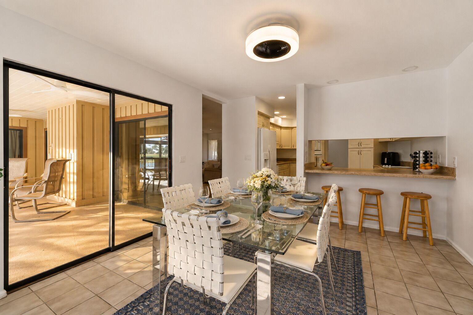 A modern dining area with a glass table, white chairs, and a kitchen in the background.