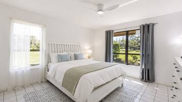 Un dormitorio con una cama, una mesita de noche, una lámpara, una ventana con cortinas y vistas al exterior.