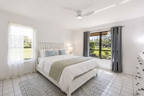 Een slaapkamer met een bed, nachtkastje, lamp, raam met gordijnen en uitzicht op de omgeving.