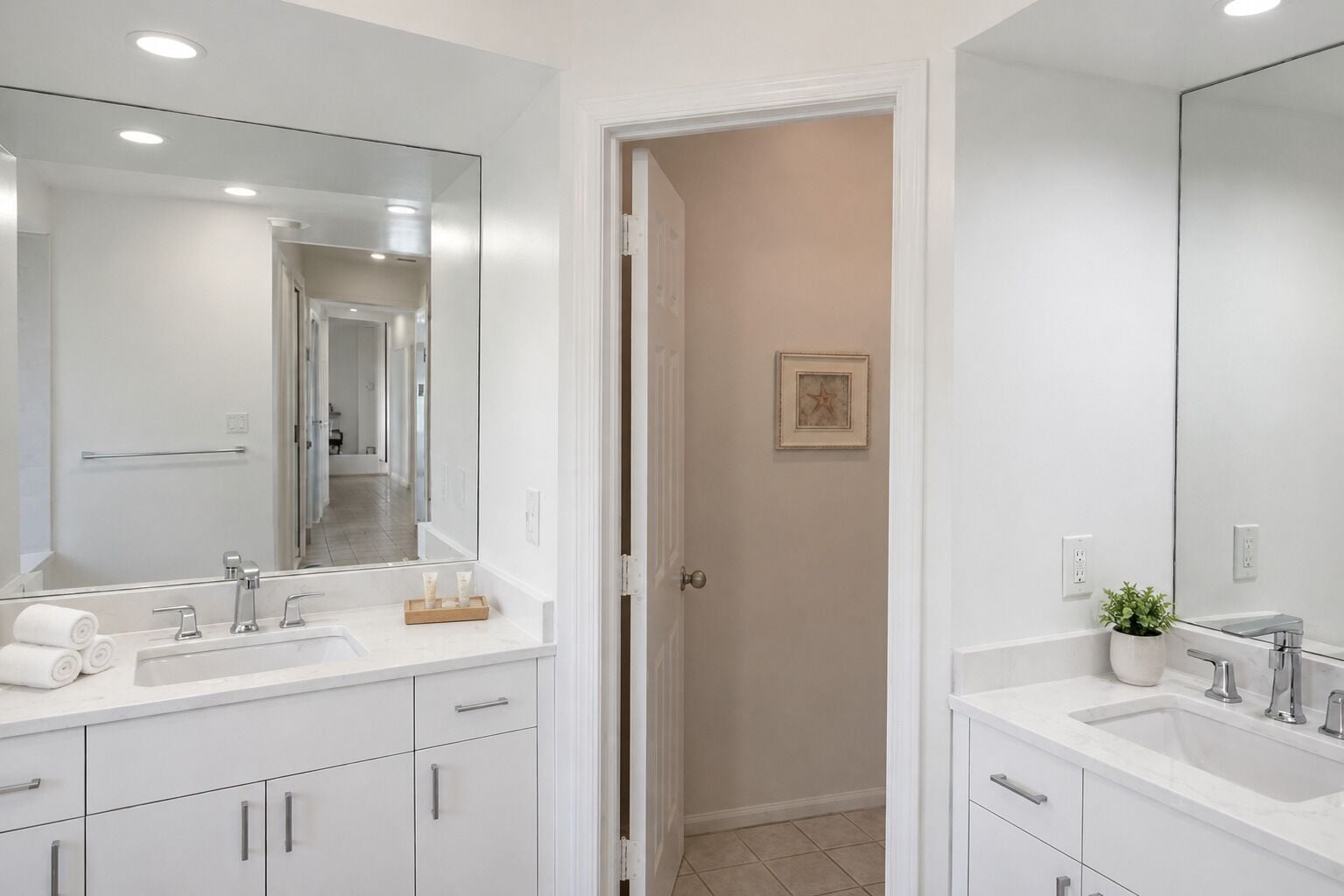Une salle de bain moderne avec deux lavabos, un grand miroir et une porte donnant sur une autre pièce.