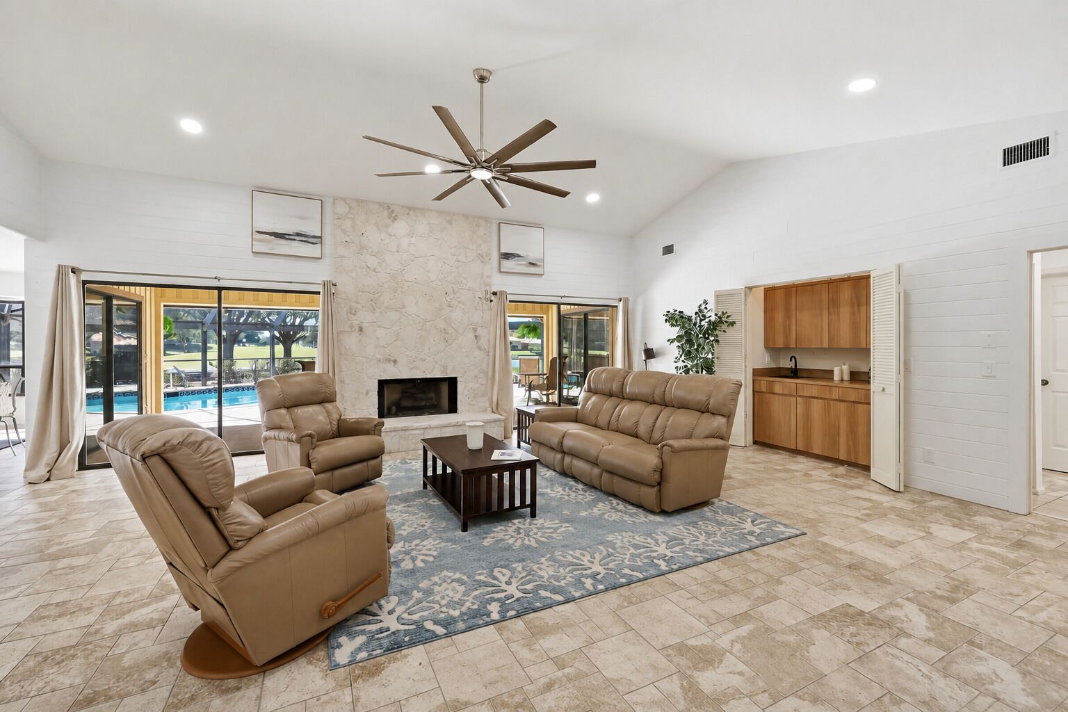 A spacious living room with leather sofas, a fireplace, and a ceiling fan.