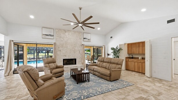 A spacious living room with leather sofas, a fireplace, and a ceiling fan. - Greenside in Palm Beach Gardens - Private Pool & Golf Course Views! (Palm Beach Gardens)