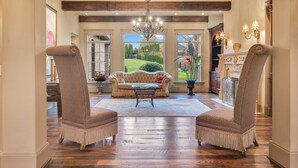 Un salon spacieux avec une grande fenêtre, un lustre et deux fauteuils.