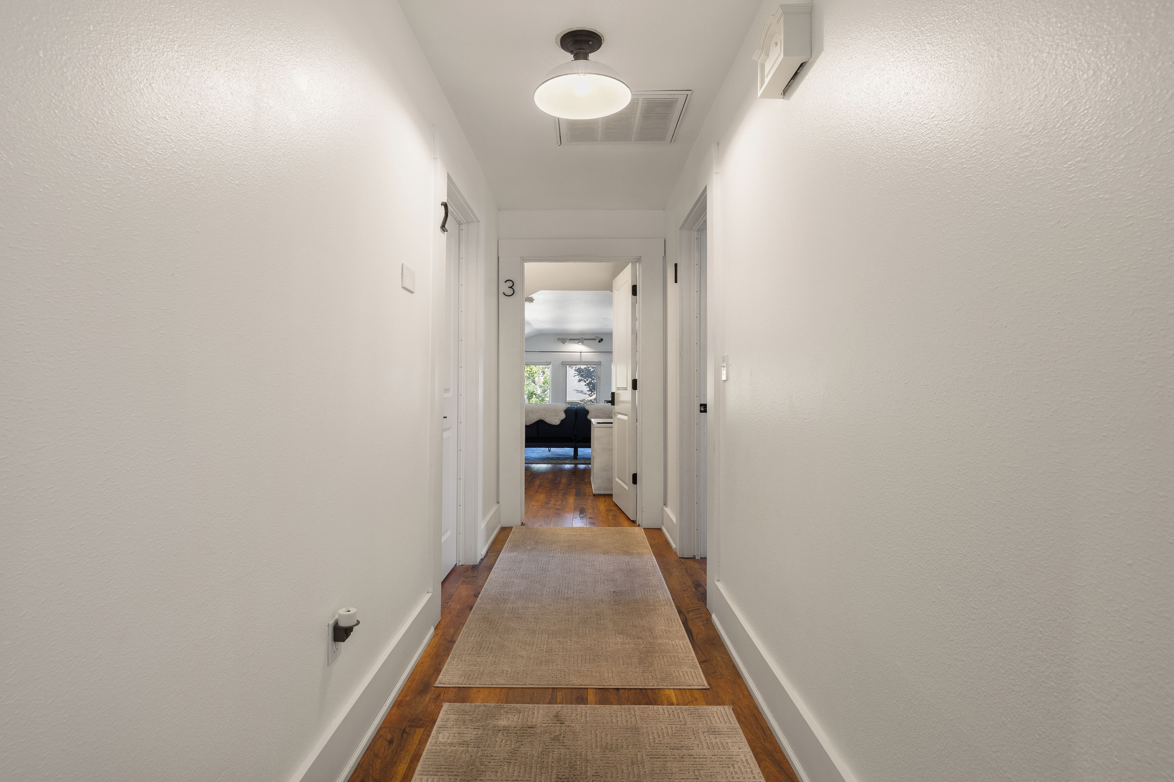 A hallway with white walls, wooden flooring, and a ceiling light fixture.