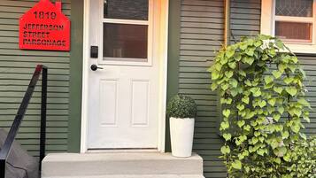 A house with a white door, a red house number sign, and a small potted plant on the steps.
