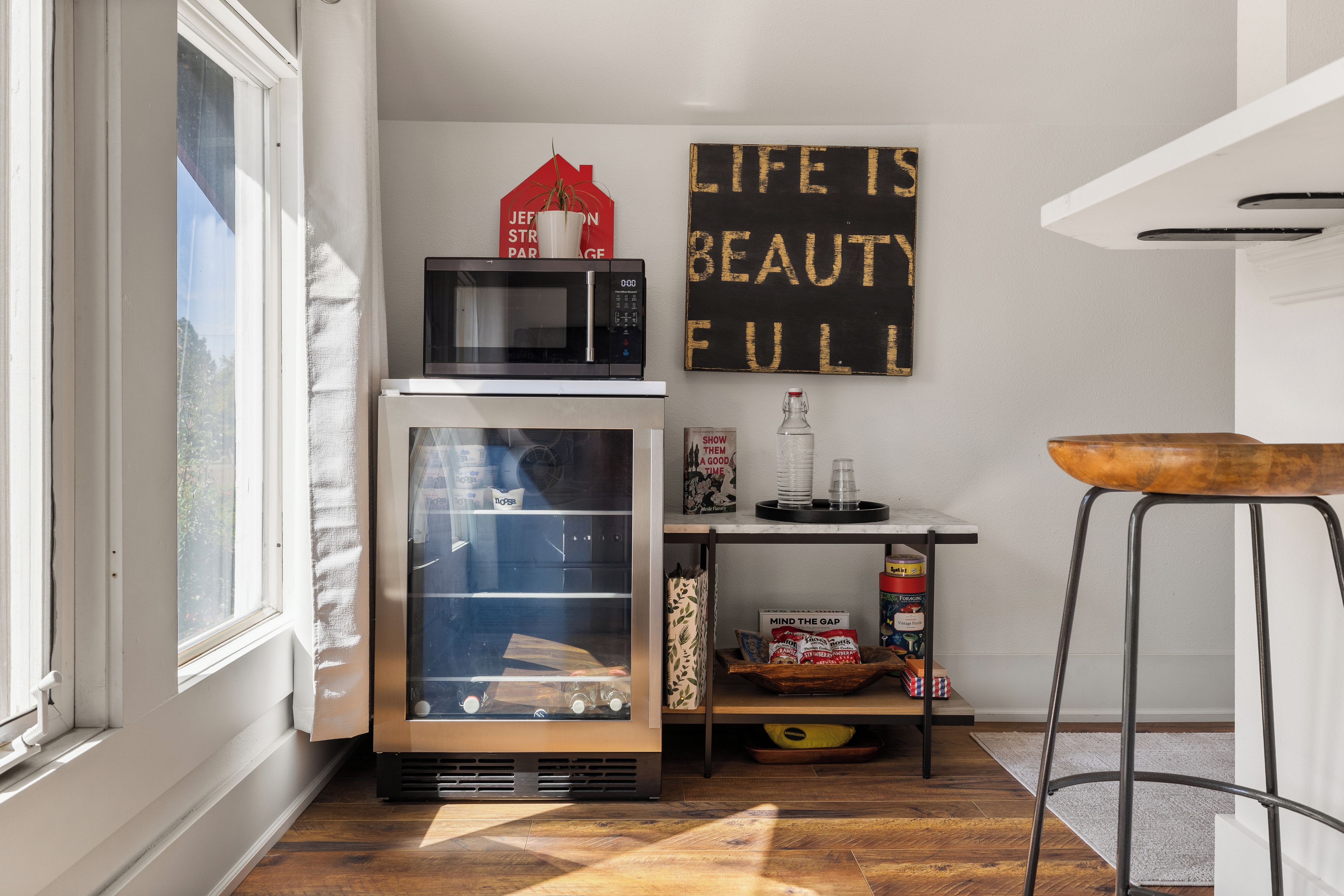 A compact kitchen with a microwave, refrigerator, and a shelf with kitchen items.