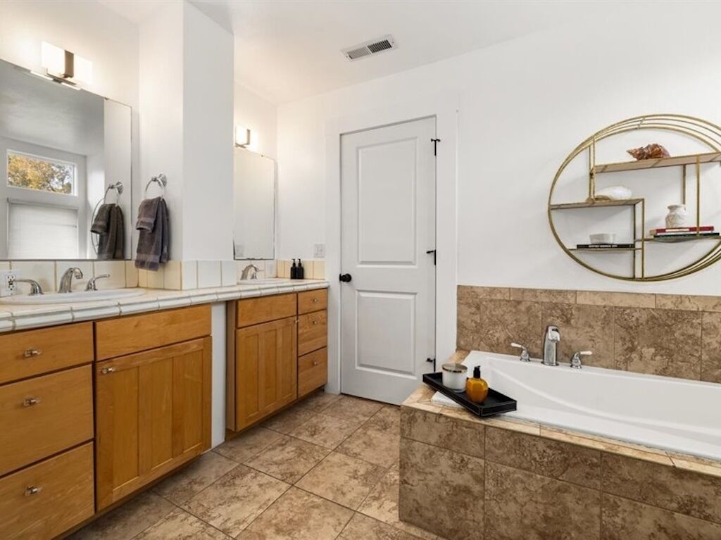 A modern bathroom with a large vanity, a bathtub, and a round shelf with toiletries.