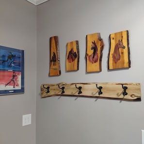 A wall with four wooden horse paintings and a wooden coat rack with hooks.