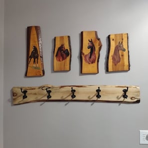 Quatre tableaux représentant des chevaux, peints sur des planches de bois, sont accrochés à un mur, et un porte-manteau en bois se trouve en dessous.
