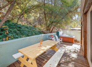 Un patio exterior con una mesa de madera y bancos, rodeado de abundante vegetación y árboles.