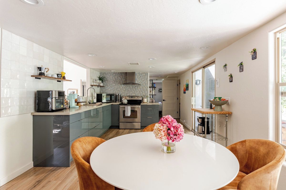Een moderne keuken met een centraal eiland, een eethoek met een ronde tafel en uitzicht op de omgeving.