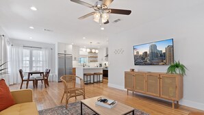 Een moderne woonkamer met een eethoek, een keuken op de achtergrond en een stadsgezicht schilderij aan de muur.