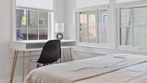 Een slaapkamer met een bed, een bureau met stoel en een raam met jaloezieën.