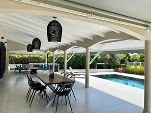 Eine überdachte Terrasse im Freien mit Pool, Essbereich und Liegestühlen.
