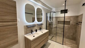Un baño moderno con tocador de madera, cabina de ducha de vidrio y dos espejos.