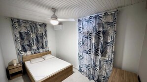 Un dormitorio con cama de madera, mesita de noche, ventilador de techo y cortinas estampadas.