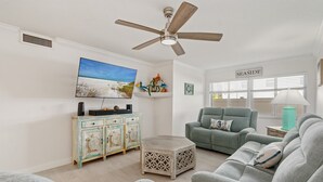 Uma sala de estar com ventilador de teto, televisão, sofá verde e mesa de centro.