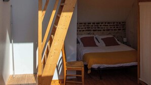 Una escalera de madera que lleva a un dormitorio en entrepiso con una cama y una silla.