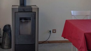 Una habitación con un estufa de leña, una silla blanca y un mantel rojo.