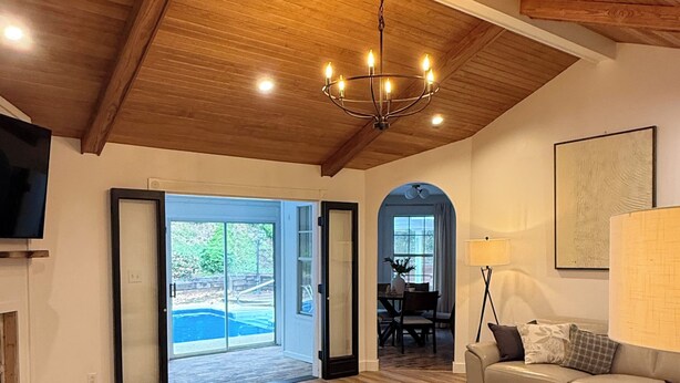 Ein geräumiges Wohnzimmer mit Holzboden, einer Chandelierleuchtre und einer Couch. Durch Glastüren ist ein Essbereich zu sehen.