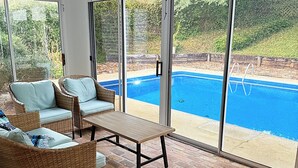 Eine sonnendurchflutete Terrasse mit Korbmöbeln, einem Deckenventilator und Blick auf einen Swimmingpool.