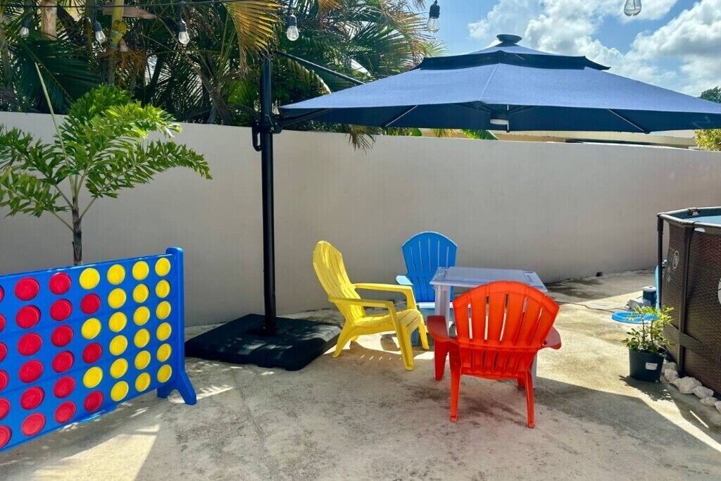 Un'area patio con un ombrellone blu, un tavolo e sedie colorate in plastica.