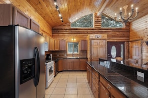 A log cabin kitchen with a refrigerator, stove, sink, and wooden cabinets. - Henry`s Fork Cabin | Steps to River, Hot Tub, Amazing Views, + BBQ! (Island Park)