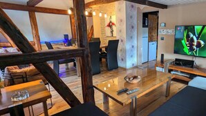 Ein modernes Wohnzimmer mit Holzboden, einem Glastisch und einem Flachbildfernseher.