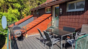 Eine Holzterrasse mit Gartenmöbeln, einem Schornstein und einem Haus mit rotem Dach.